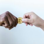 Two hands exchanging a Bitcoin coin, symbolizing cryptocurrency transactions.